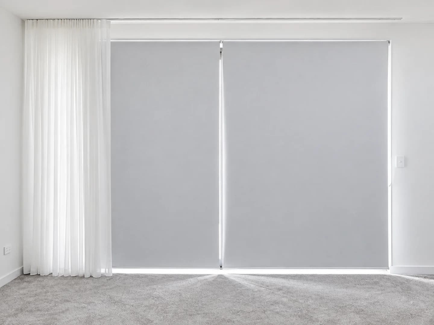 Two pale grey blockout roller blinds beside a white sheer curtain