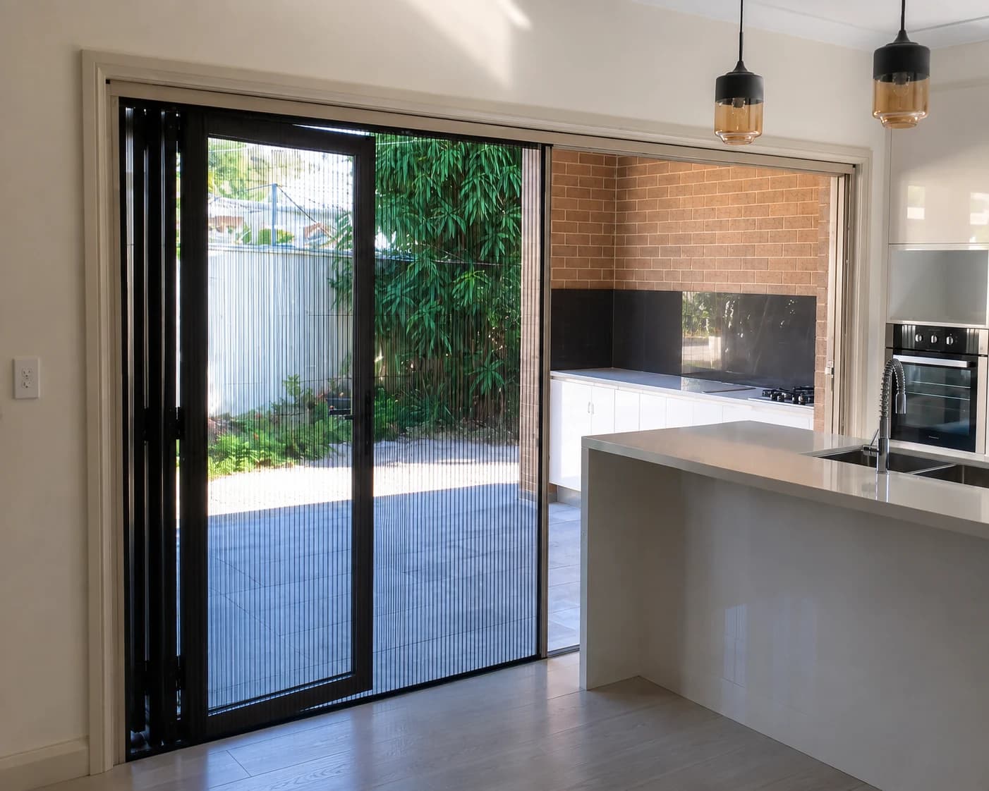 Pleated retractable fly screen across a wide kitchen opening to an alfresco patio