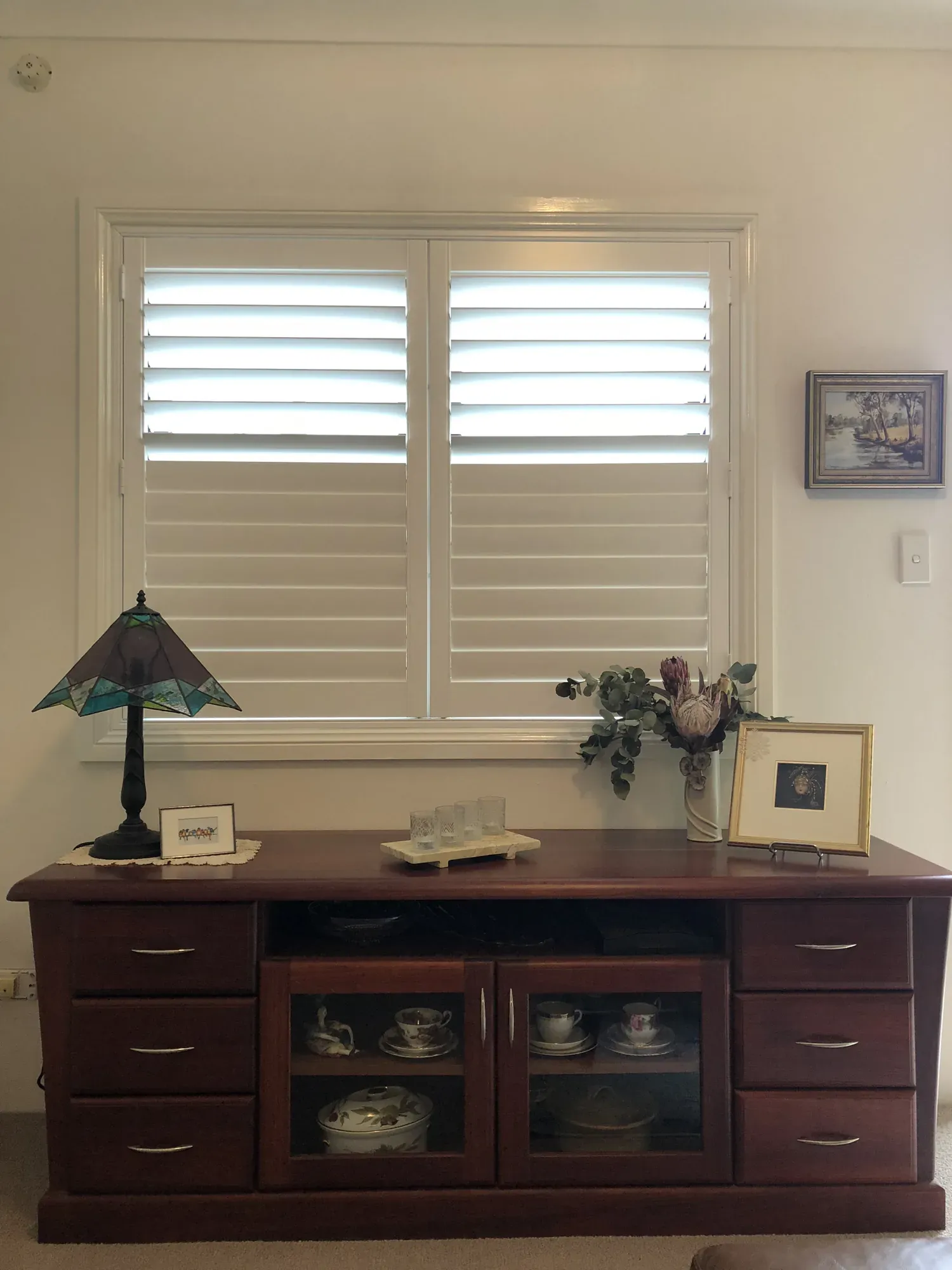 White plantation shutters fitted to an interior window above a timber sideboard.