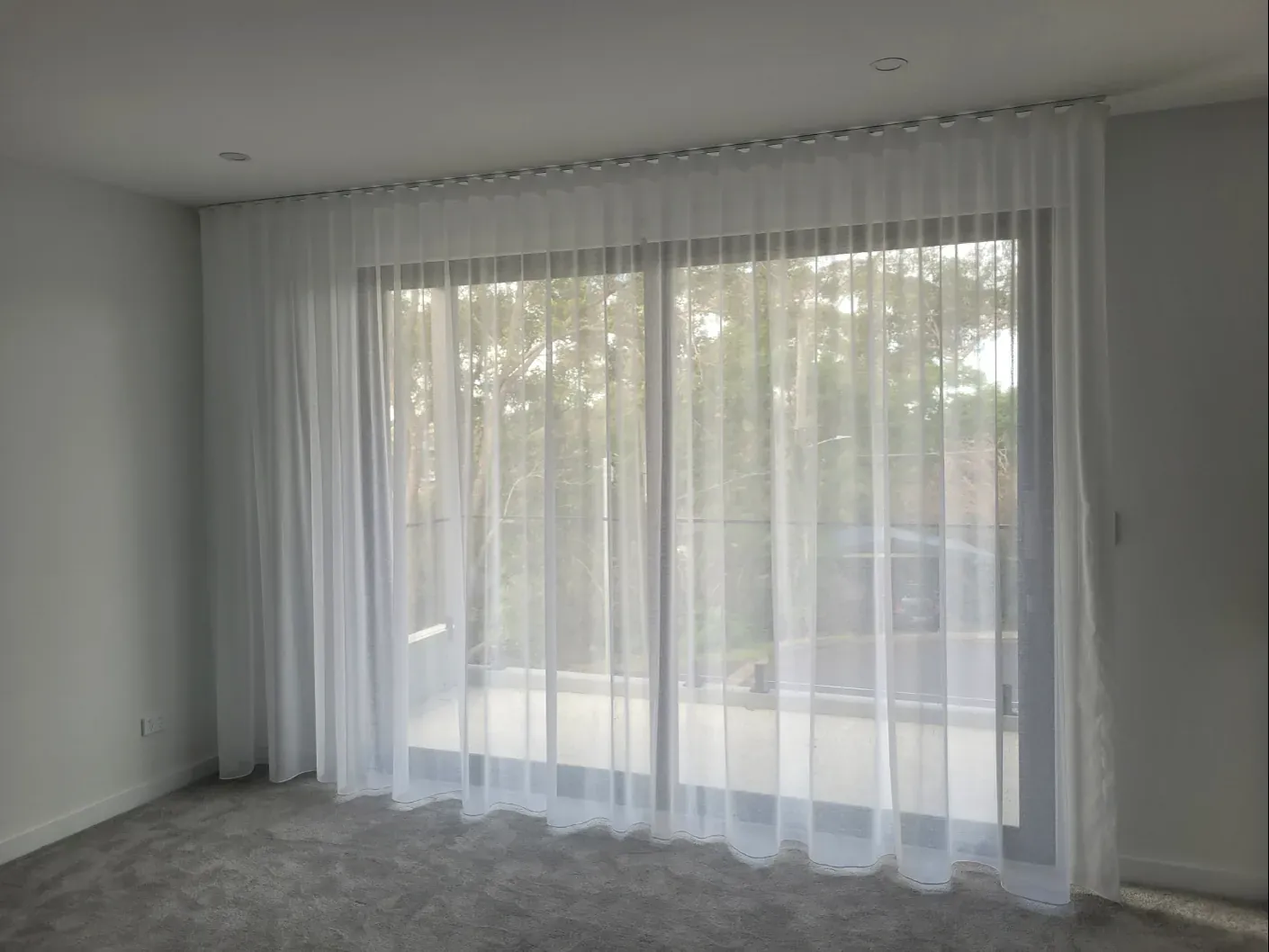 Floor-to-ceiling white sheer curtains installed across a wide sliding glass door.