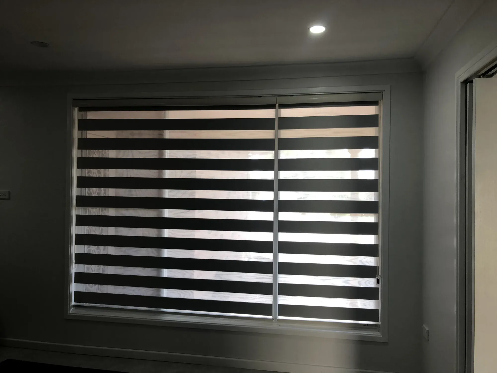 Zebra blinds fitted to a wide living room window with alternating dark opaque and sheer horizontal bands.