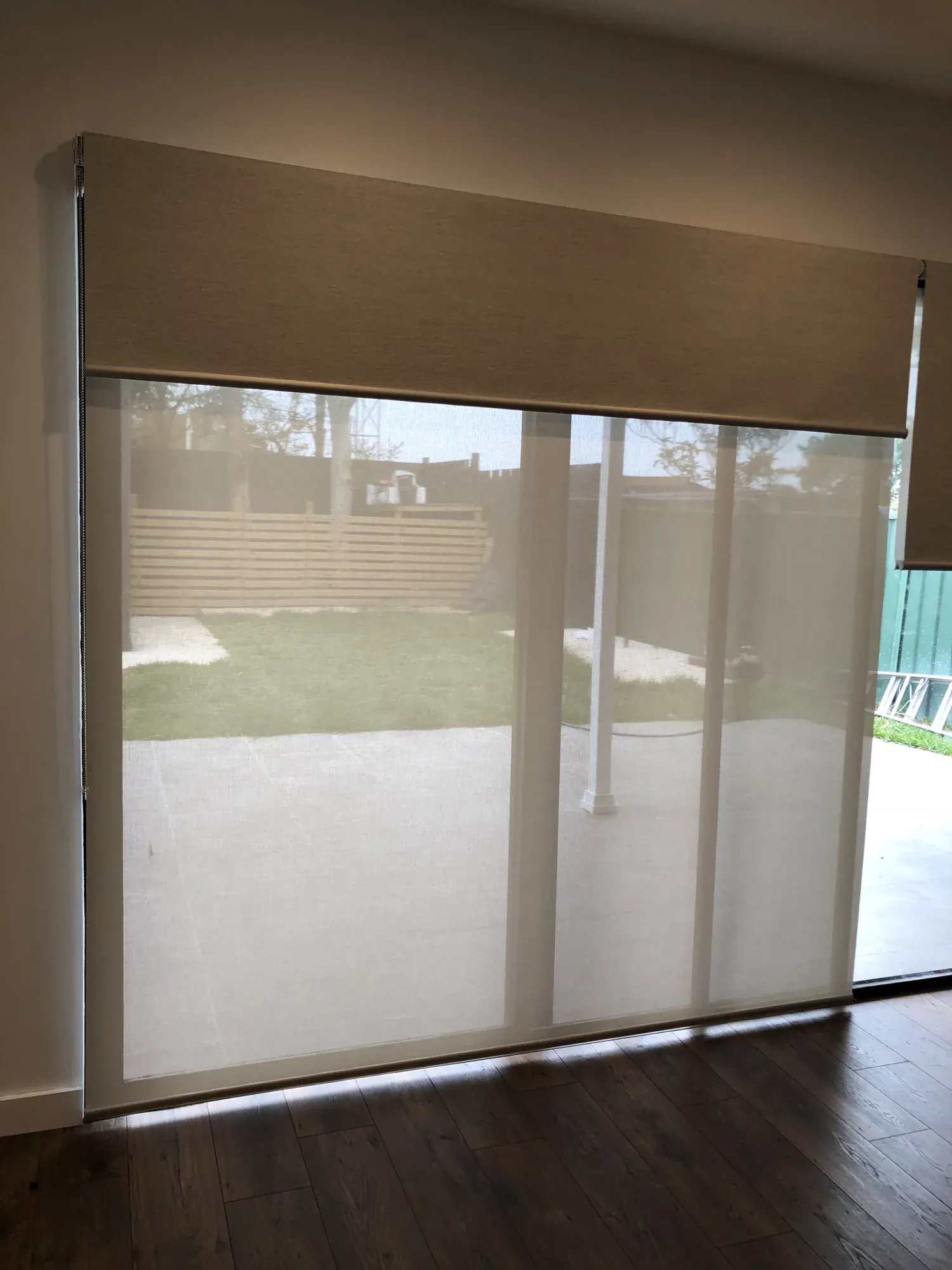Dual roller blinds combining a translucent sunscreen layer with a blockout blind over a wide glass door.